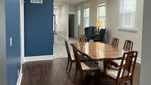 A dining area with a wooden table and chairs, a blue accent wall, and a kitchen in the background. - 1890's Craftsman Home 5BR 4BA, Sleeps 16+ w 6 TVs. (Omaha)