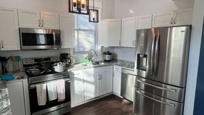 A modern kitchen with white cabinets, stainless steel appliances, and a built-in oven. - 1890's Craftsman Home 5BR 4BA, Sleeps 16+ w 6 TVs. (Omaha)