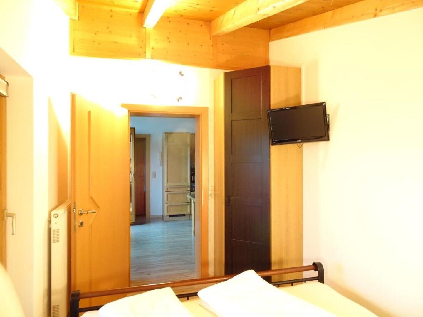 A bedroom with a bed, a television mounted on the wall, and a wooden ceiling.