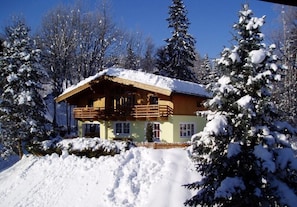 Una cabaña de madera con balcón, rodeada de árboles cubiertos de nieve.