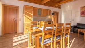 Una mesa de comedor de madera con sillas, una zona de cocina con armarios de madera y un sofá negro en una habitación con suelo de madera y techo inclinado.