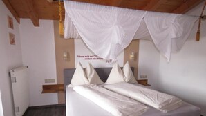 Un dormitorio con una cama, cortinas blancas, un reloj de pared y un radiador.