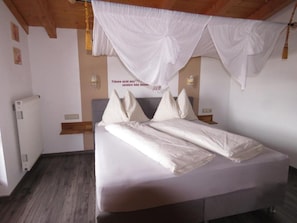 Un dormitorio con una cama, cortinas blancas, un reloj de pared y un radiador.