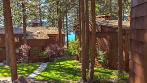 A wooden cabin with a stone pathway leading to a deck, surrounded by trees and a view of a body of water. - Modern Condo | Private Beach & Decks | Sleeps 8 (Zephyr Cove)