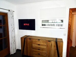 Een kamer met een houten console tafel, een flatscreen televisie aan de muur en een ingelijste foto erboven.