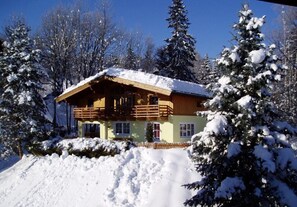 Een houten chalet met balkon, omringd door met sneeuw bedekte bomen.