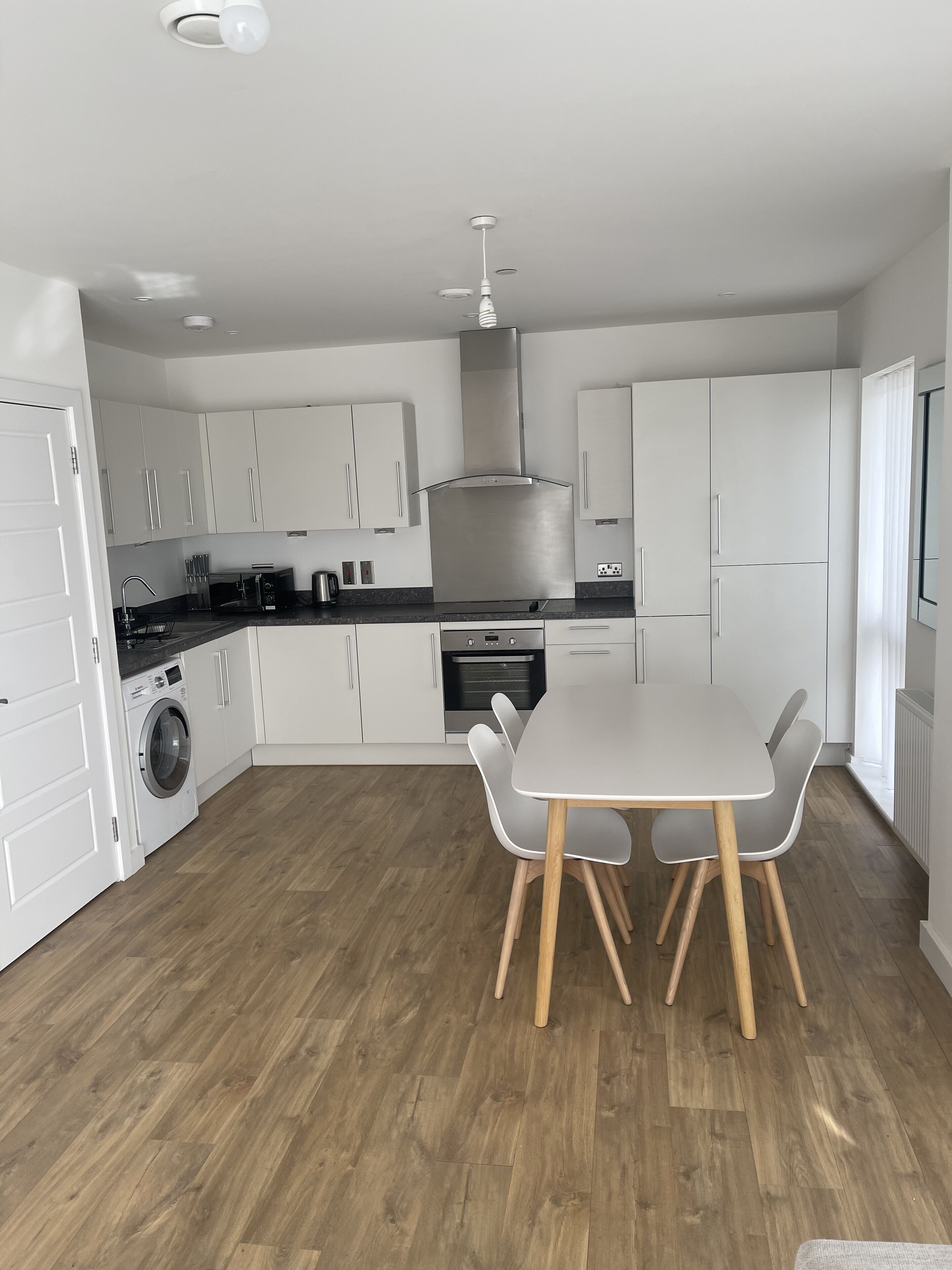 A modern kitchen with white cabinets, a built-in oven, and a dining area with a table and chairs.