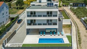 Un edificio moderno de varios pisos con piscina en la azotea, un espacio al aire libre techado con asientos y vistas del paisaje circundante.