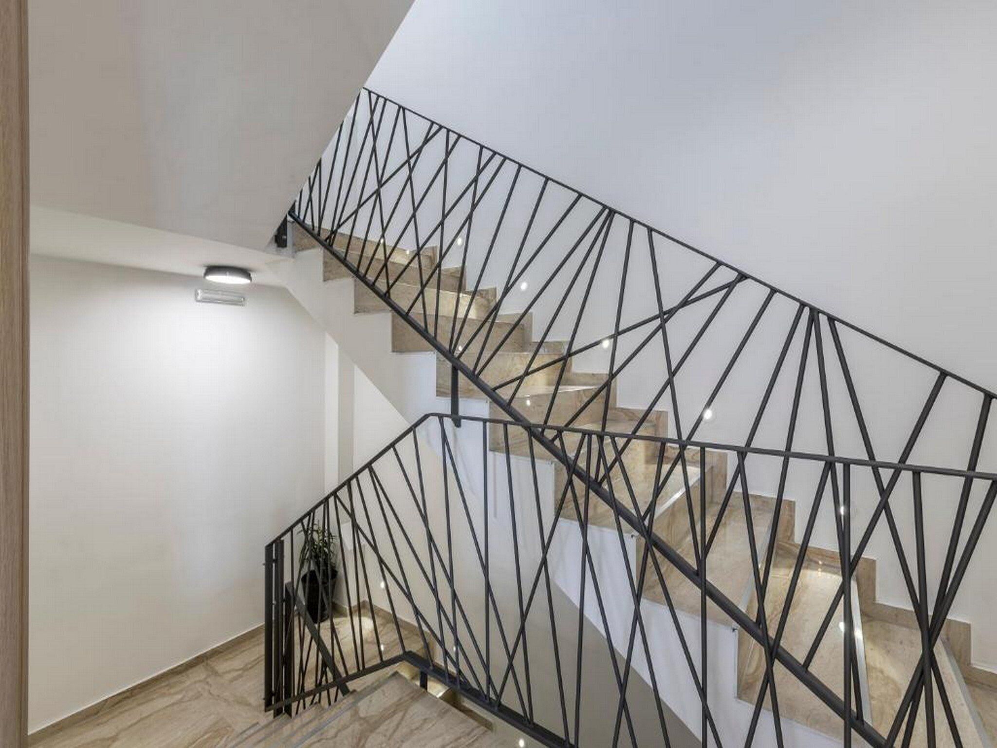 A modern staircase with a geometric metal railing and a light-colored wall.