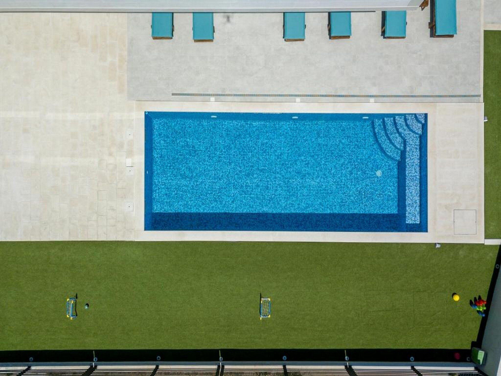 Piscina rectangular con interior azul, rodeada por un deck de color claro y una zona de césped verde.