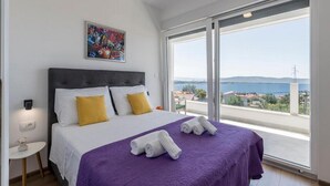 A bedroom with a large bed, a view of the sea, and a painting on the wall.