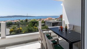 A balcony with a table and chairs, overlooking a coastal view with buildings and a body of water.