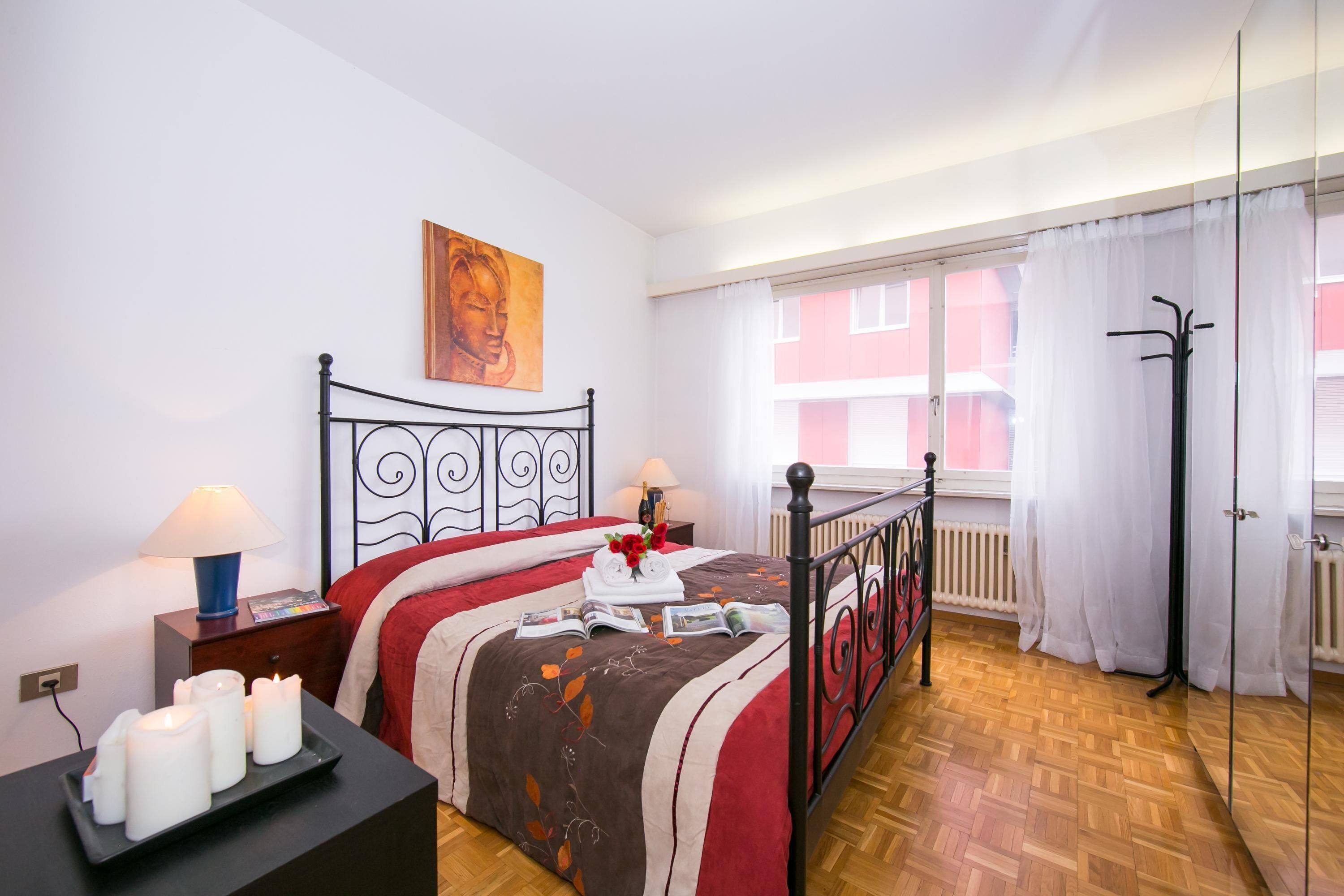 A bedroom with a bed, bedside lamps, a window with curtains, and a radiator.
