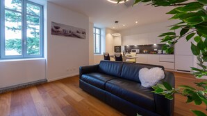 A modern living room with a black leather sofa, a white fluffy pillow, and a large window overlooking a kitchen area. - Love of Lugano in Lugano (Lugano)
