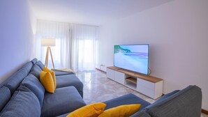 A modern living room with a grey sofa, yellow cushions, a flat-screen TV, and a floor lamp.