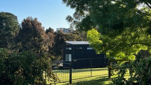 A modern, dark-colored building with a flat roof, surrounded by lush greenery and trees. - Merricks North Tiny House (Merricks North)