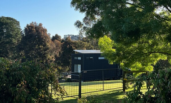 A modern, dark-colored building with a flat roof, surrounded by lush greenery and trees.