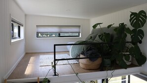 A room with a bed, a window, and a plant stand. - Merricks North Tiny House (Merricks North)