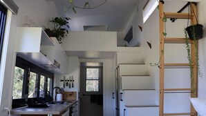 A compact kitchen with a central island, a wooden ladder, and hanging plants. - Merricks North Tiny House (Merricks North)