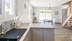 Een moderne keuken met een groot raam, een eethoek met een tafel en stoelen, en een trap naar een ander niveau.