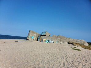 A beach with large concrete structures covered in graffiti, a clear blue sky, and the ocean in the background.