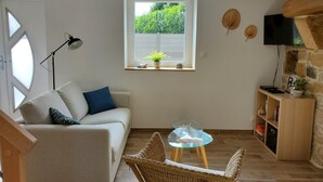 Een gezellige woonkamer met een bank, een glazen tafel, rieten stoelen, een televisie en een stenen muur.
