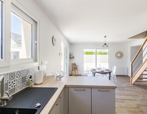 A modern kitchen with a large window, a dining area with a table and chairs, and a staircase leading to another level. - Modern house near Barfleur with private garden (Saint-Pierre-Église)