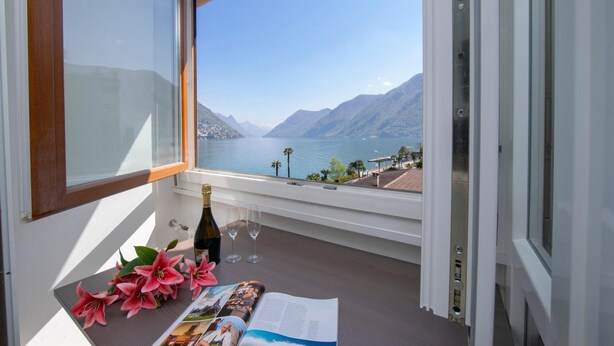 A balcony with a view of a lake and mountains, a bottle of wine, two glasses, and a magazine. - Paradiso Incanto in Paradiso Lugano (Paradiso)
