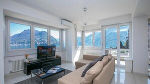 A modern living room with a large TV, comfortable seating, and large windows offering mountain views. - Paradiso Incanto in Paradiso Lugano (Paradiso)