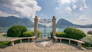A garden with a stone bench, a decorative gate, and a view of a lake with mountains in the background. - Paradiso Incanto in Paradiso Lugano (Paradiso)