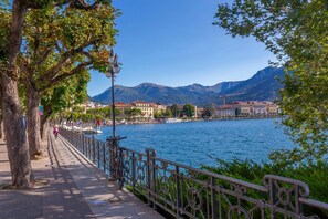 A waterfront promenade with a metal railing, trees, and buildings in the background. - Fairy Home in Viganello Lugano (Lugano)
