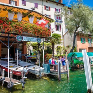 A waterfront restaurant with outdoor seating, boats docked nearby, and a clear view of the water. - Fairy Home in Viganello Lugano (Lugano)