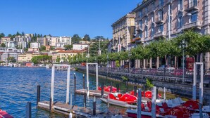 A waterfront area with red paddle boats docked at a pier, a stone bridge, and buildings with balconies. - Fairy Home in Viganello Lugano (Lugano)