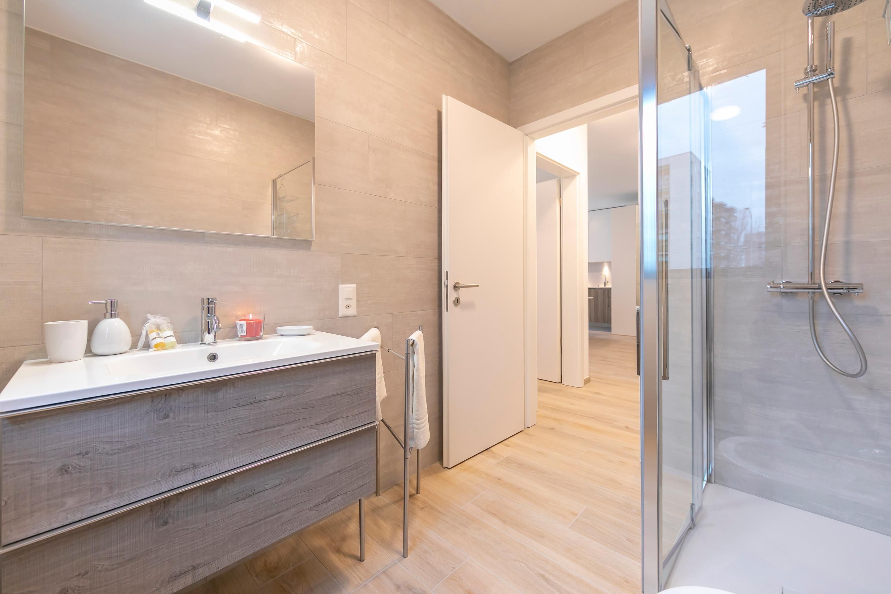 A modern bathroom with a large mirror, a white sink, a wooden vanity, and a glass shower enclosure.