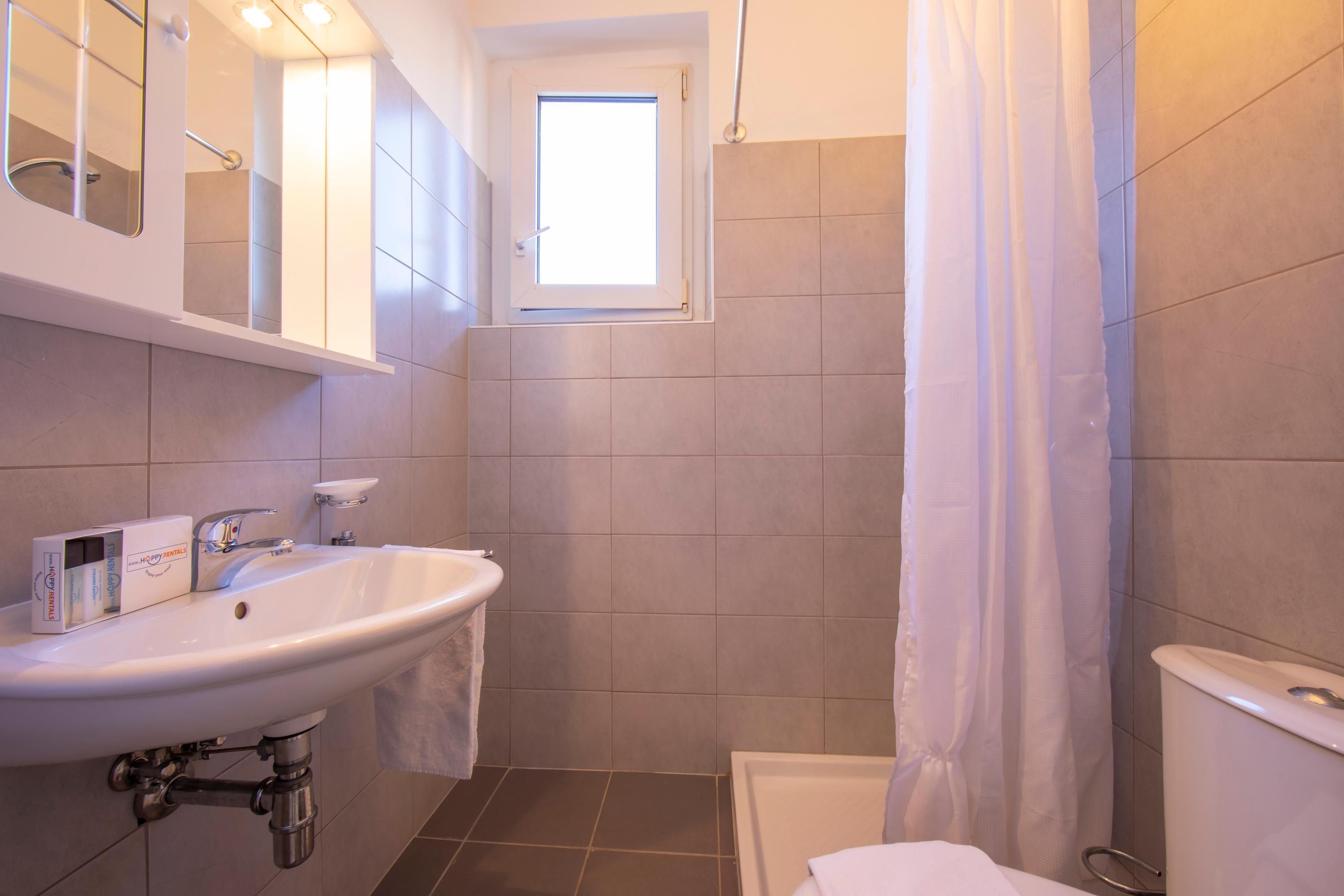 A bathroom with a sink, mirror, window, shower, and toilet.