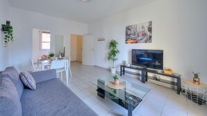 A modern living room with a sofa, a glass coffee table, a TV, and a dining area with chairs and a table. - Central Amor in Lugano (Lugano)