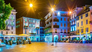 A brightly lit square with outdoor seating, surrounded by historic buildings with balconies and awnings. - Central Amor in Lugano (Lugano)