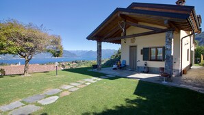 A small house with a stone facade, a wooden roof, and a stone pathway leading to the entrance. - Villa Giorgia Private Pool (Castelveccana)