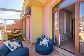 Ein Balkon mit zwei blauen Sitzsäcken, einem Tisch mit Stühlen und einer Glastür zu einem Holzkasten.