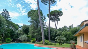 A swimming pool with lounge chairs and a table, surrounded by trees and a house.
