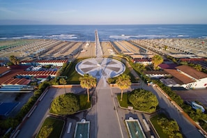 Une vue aérienne d’une station balnéaire avec une place circulaire centrale, plusieurs villas situées en bord de mer et une longue jetée qui s’avance dans l’océan.