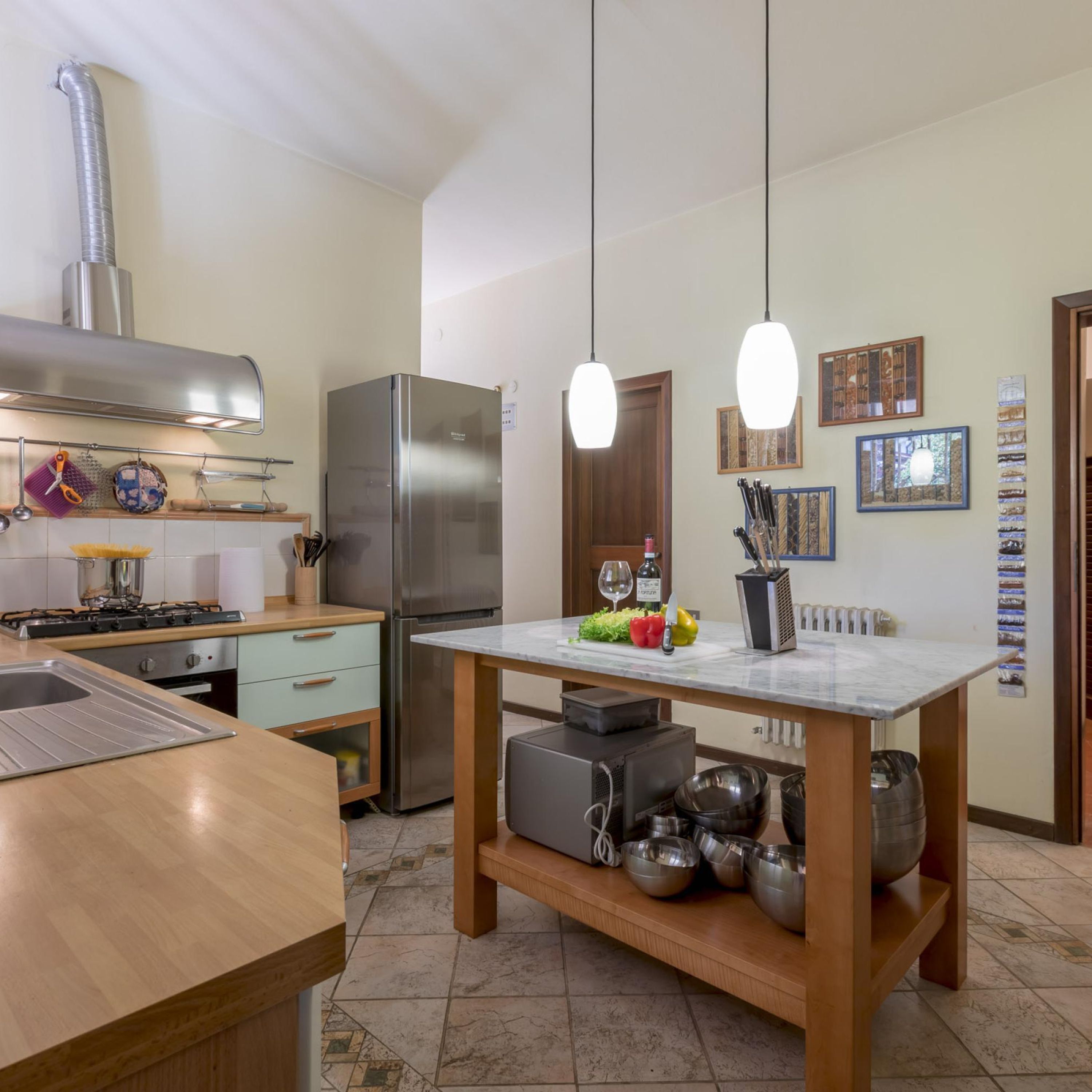 A modern kitchen with a stainless steel refrigerator, a gas stove, and hanging pendant lights.
