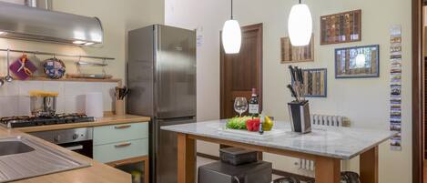 A modern kitchen with a stainless steel refrigerator, a gas stove, and hanging pendant lights.