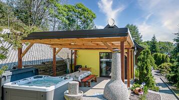 Ein Whirlpool, eine Holzpergola und eine Steinskulptur in einem Garten mit gelber Wand und Holzterrasse.