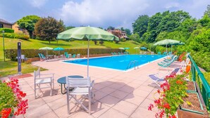 A swimming pool with lounge chairs and umbrellas, surrounded by greenery and a hilly landscape. - Residenza La Parusciola (Gignese)