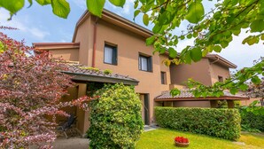 A two-story building with a flat roof, a covered patio area, and a well-maintained garden with a lawn, a flower bed, and a hedge. - Residenza La Parusciola (Gignese)