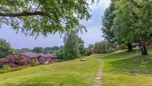 A grassy area with a pathway leading to a house, surrounded by trees and greenery. - Residenza La Parusciola (Gignese)