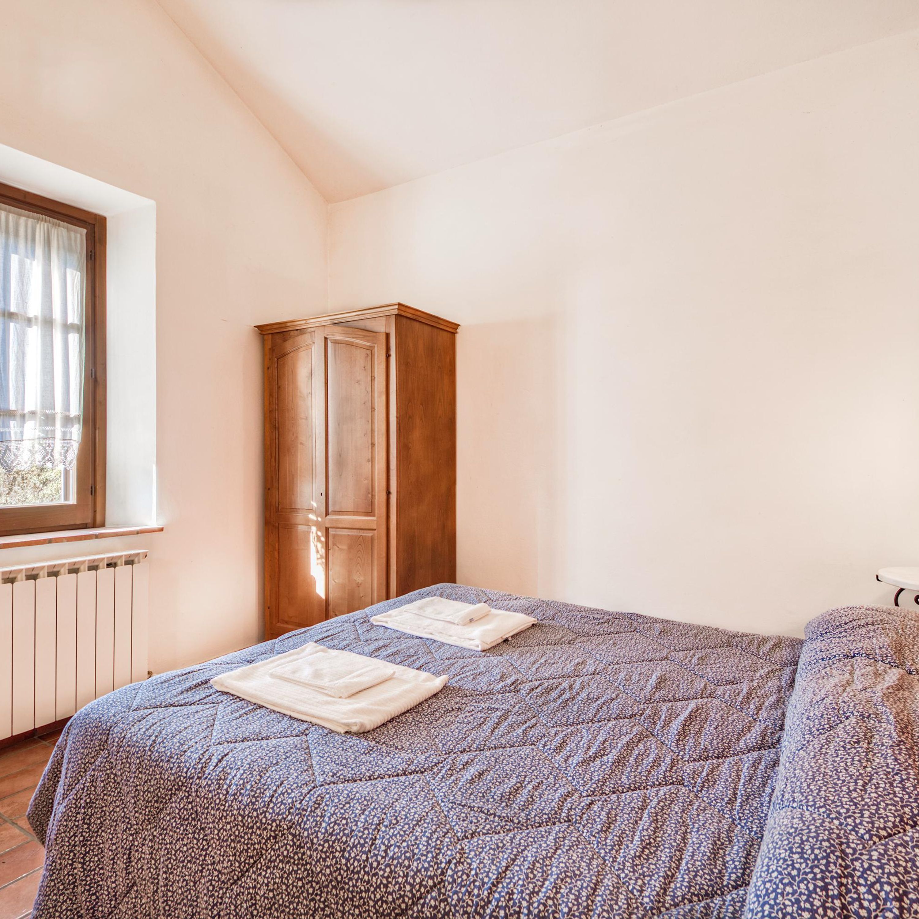 A bedroom with a bed, a wardrobe, a window, and a radiator.
