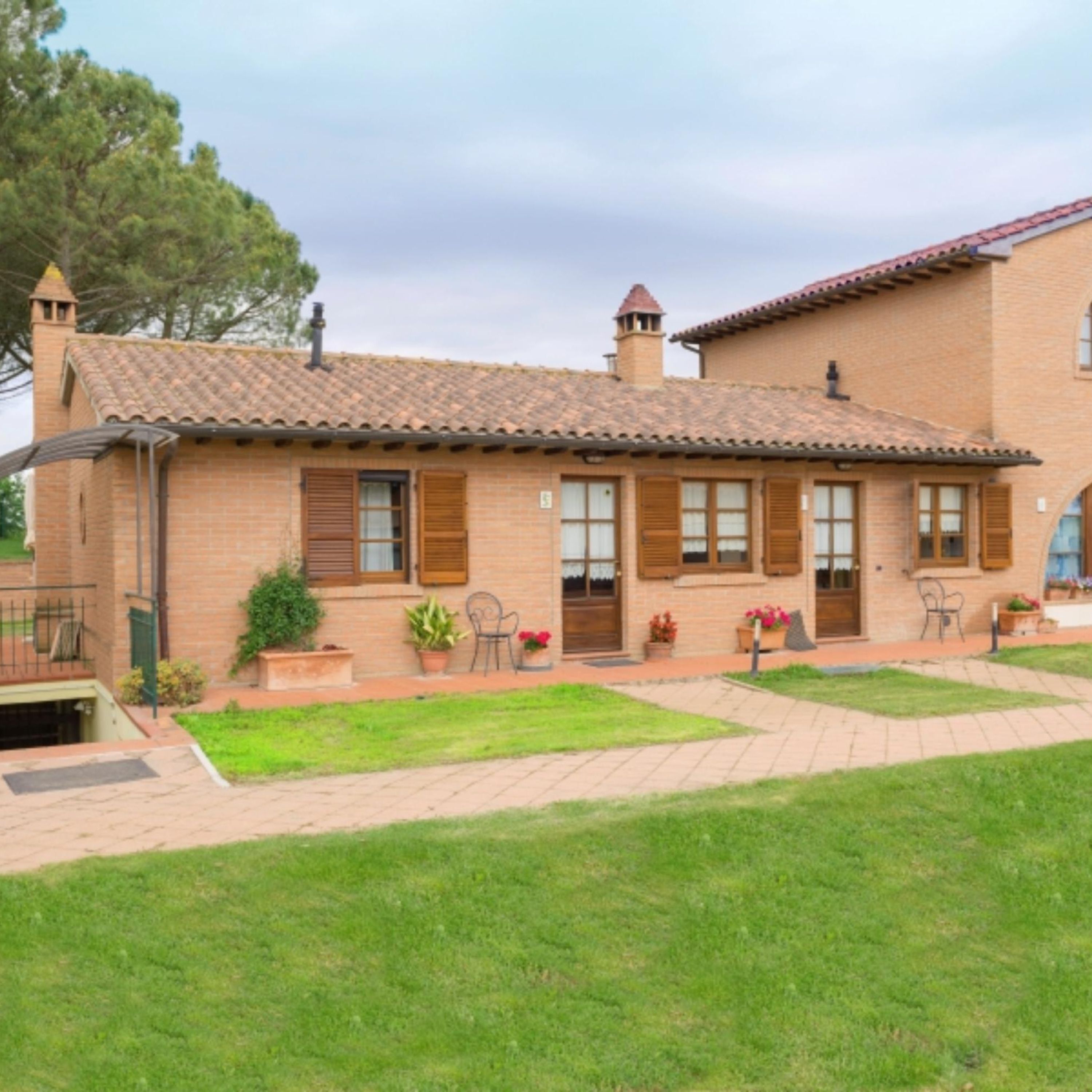Una casa a due piani in mattoni con tetto in tegole, un piccolo garage adiacente e vialetto lastricato.