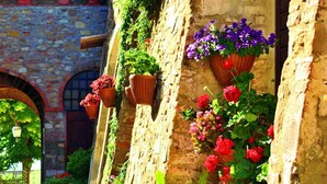 A narrow stone pathway flanked by walls adorned with hanging flower pots containing a variety of flowers. - La Badia 2 in Tavarnelle Val di Pesa (Barberino Tavarnelle)